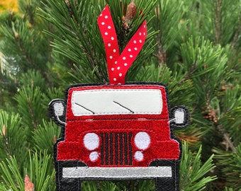 Pode incluir: Adorno de Jeep vermelho com glitter, pára-brisa branco e faróis brancos. O adorno está pendurado em uma fita vermelha com bolinhas brancas.