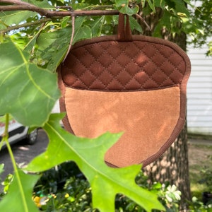 Puede incluir: Un posavasos con forma de bellota marrón y beige con la parte superior acolchada y la inferior suave y peluda.