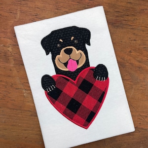 May include: Embroidered design of a black and brown dog holding a red and black buffalo plaid heart.