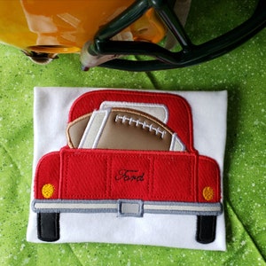 May include: Red toy pickup truck with a brown football in the bed. The truck has a white "Ford" logo on the back.