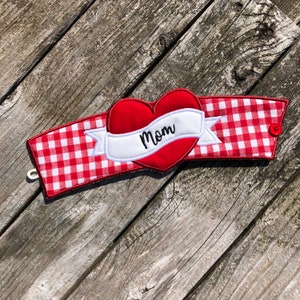 May include: Red and white gingham fabric coffee cup cozy with a red felt heart and a white banner that says "Mom".