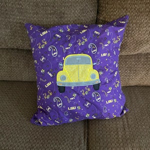 May include: Purple pillow with a yellow Volkswagen Beetle design and the letters "LSU" repeated throughout the fabric.