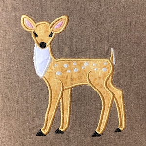 May include: A brown and white embroidered fawn with white spots on a brown fabric background.