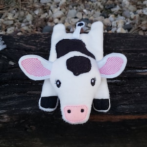 May include: A white and black plush cow with pink ears and nose. The cow is lying on its belly with its legs outstretched.