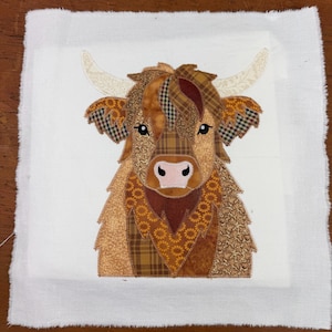 Pode incluir: Uma peça de arte têxtil com uma vaca das Terras Altas. A cabeça da vaca é feita de vários tecidos estampados em tons de castanho, bege e creme. Possui chifres grandes e curvos e um nariz rosa. A obra de arte está sobre um fundo branco.