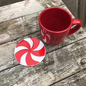 May include: A red and white peppermint candy-shaped coaster with a red mug on a wooden surface.