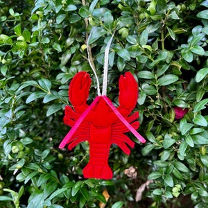 May include: Red felt lobster ornament with a white string for hanging. The lobster is detailed with black stitching.