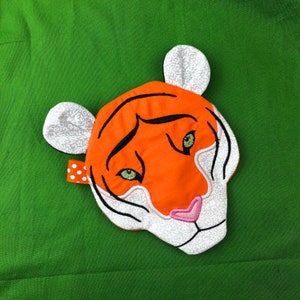 May include: Orange and white embroidered tiger face with green eyes. The tiger face is a soft, plush fabric and would be great for a child's room or play area.