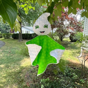 May include: A white and green ghost-shaped baby blanket with a smiling face and green eyes. The blanket is made of soft, plush fabric and has a textured surface.
