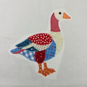 May include: A colorful patchwork goose applique with a white background. The goose features a red and white polka dot body, blue and white patterned wings, and a red and white checkered neck. The beak is orange.