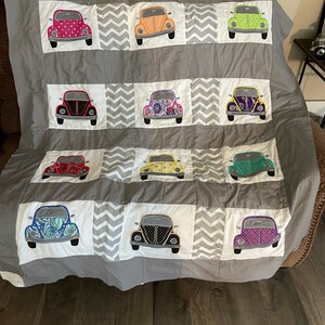 May include: A gray quilt with a chevron pattern features 12 embroidered Volkswagen Beetle cars in various colors and patterns.