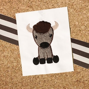 May include: Embroidered design of a brown and gray cartoon bison with a brown fluffy mane, sitting with its legs crossed.