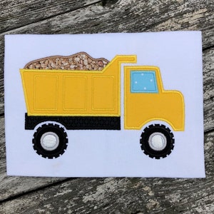 May include: A yellow toy dump truck with a black chassis and black tires. The truck bed is filled with brown dirt and has a blue window.