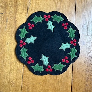 May include: A black felt Christmas wreath with green holly leaves and red berries.
