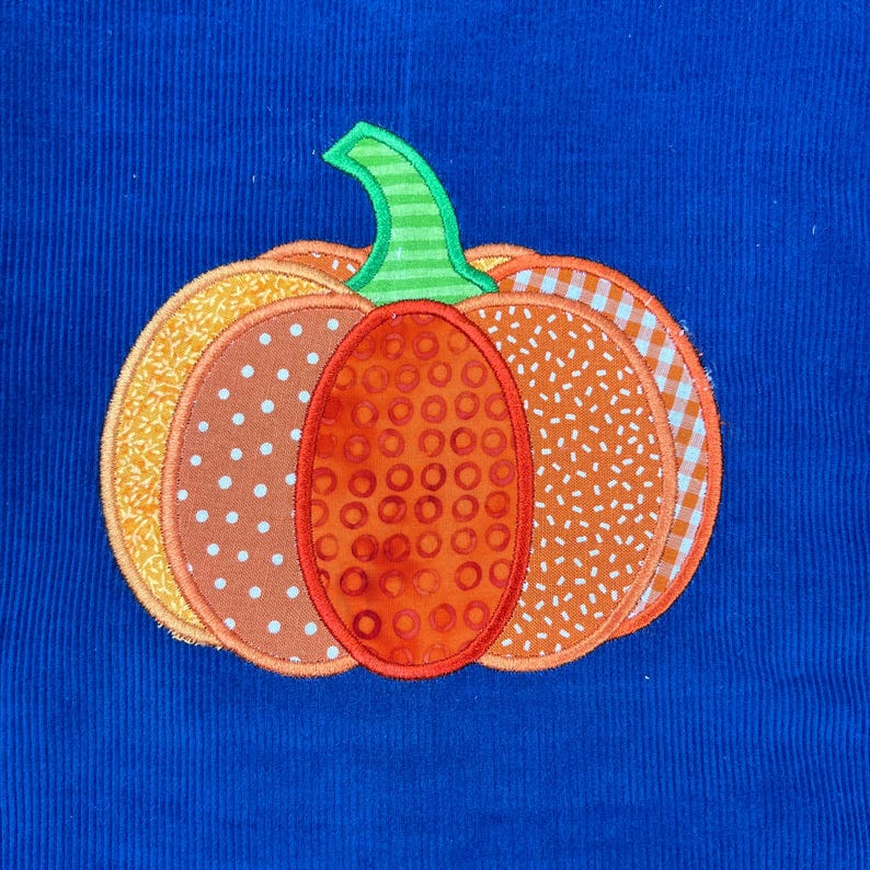 May include: A decorative pumpkin applique featuring orange, yellow, and brown patterned sections, and a green stem. The pumpkin is set against a vibrant blue corduroy background, ideal for autumn decorations.