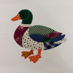May include: A patchwork duck with a green plaid head, an orange beak with white polka dots, and a body made of various patterned fabrics. The duck's body includes floral, plaid, and dotted patterns, with orange feet. The background is plain white.