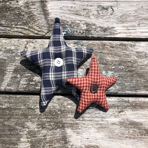 May include: Two fabric stars with buttons in the center. The larger star is blue and white plaid, and the smaller star is red and white gingham.