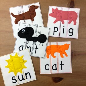 May include: A set of five felt puzzles featuring animal silhouettes and the corresponding word spelled out below. The animals are a sun, a cat, a pig, an ant, and a dachshund. The puzzles are designed for children to learn their first words.