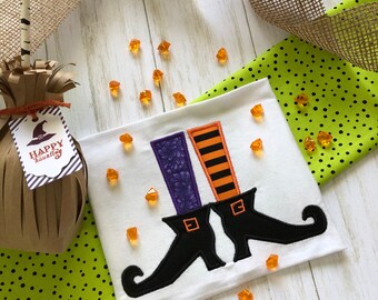 May include: White fabric with a black and purple witch's boot design. The fabric has the text "Happy Haunting" on a tag attached to it.