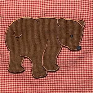 May include: A brown embroidered bear applique on a red and white gingham fabric.