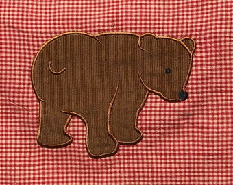 May include: A brown embroidered bear applique on a red and white gingham fabric.