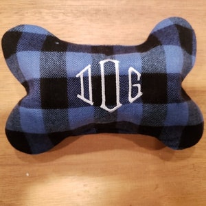 May include: A blue and black checked dog bone shaped cushion with the word "DOG" embroidered in white.