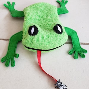 May include: A green felt frog with a long red tongue and a black fly on the end. The frog has large black eyes with white pupils.