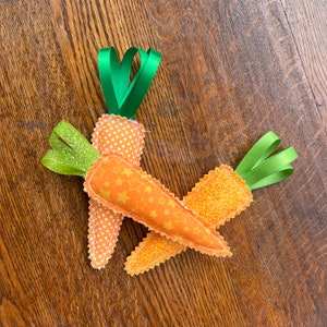 May include: Two felt carrot ornaments with green ribbon stems. One carrot has a white polka dot pattern and the other has a yellow star pattern.