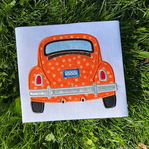 May include: Orange and white polka dot embroidered applique of a vintage Volkswagen Beetle car. The car is facing away from the viewer and has a blue license plate.