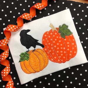 May include: A black crow perched on top of an orange pumpkin with a green leaf. A larger orange pumpkin with white polka dots is behind the crow and pumpkin.