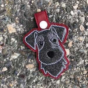 Może przedstawiać: Czarny i srebrny brelok do kluczy z psem z brokatem i czerwonymi szwami. Pies ma czarny nos i białe oczy.