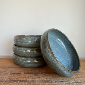 May include: Four blue and brown ceramic bowls stacked on top of each other. The bowls have a speckled glaze and a slightly rippled texture.