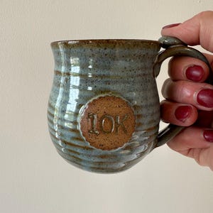 May include: A blue and brown ceramic mug with a brown circle on the side that says "10K".