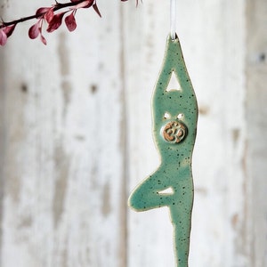 May include: A green ceramic ornament shaped like a person in a yoga pose with an Om symbol on the chest.