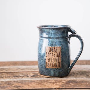May include: A blue ceramic mug with a brown rectangular label that reads "Lokah Samastah Sukhino Bhavantu".