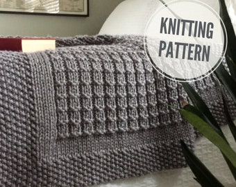 May include: A gray knitted throw blanket with a textured pattern. The blanket is folded and placed on a white bed with a plant in the background. The text "Knitting Pattern" is written in a circle on the image.
