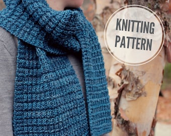 Può includere: Una sciarpa di lana blu con un motivo testurizzato. La sciarpa è indossata da una persona in piedi davanti a un betulla. Il testo "Knitting Pattern" è scritto in un cerchio sull'albero.