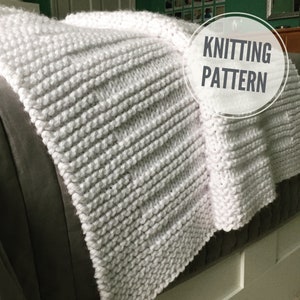 May include: White knitted blanket with a ribbed texture. The blanket is folded and draped over a couch. The text "Knitting Pattern" is written in a circle on the image.