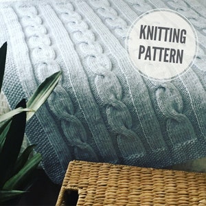 May include: A close-up of a light blue knitted throw with a cable knit pattern. The throw is soft and fluffy, and it would be perfect for snuggling up on the sofa.