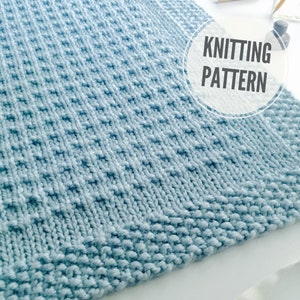 Puede incluir: Una manta de punto azul claro con un patrón de punto texturizado. La manta está hecha con un hilo suave y tiene un brillo sutil.  "Knitting Pattern" está escrito en texto blanco sobre un círculo blanco.