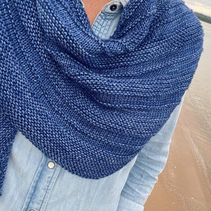 Op de afbeelding: Een blauwe gebreide sjaal met een textuurpatroon. De sjaal is gedrapeerd over een lichtblauw spijkeroverhemd. Het breiwerk heeft een gradi&euml;nteffect, dat overgaat van een donkerdere naar een lichtere blauwtint.