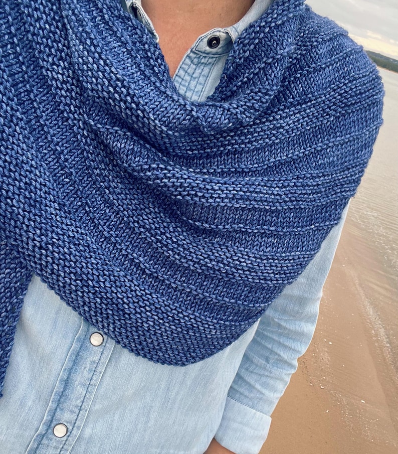 Op de afbeelding: Een blauwe gebreide sjaal met een textuurpatroon. De sjaal is gedrapeerd over een lichtblauw spijkeroverhemd. Het breiwerk heeft een gradi&euml;nteffect, dat overgaat van een donkerdere naar een lichtere blauwtint.
