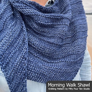 Op de afbeelding: Een blauw-witte gebreide sjaal met een textuurontwerp. De sjaal is over de schouders gedrapeerd en heeft de tekst "Morning Walk Shawl" en "Knitting Pattern by Fifty Four Ten Studio".