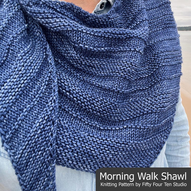 Op de afbeelding: Een blauw-witte gebreide sjaal met een textuurontwerp. De sjaal is over de schouders gedrapeerd en heeft de tekst "Morning Walk Shawl" en "Knitting Pattern by Fifty Four Ten Studio".