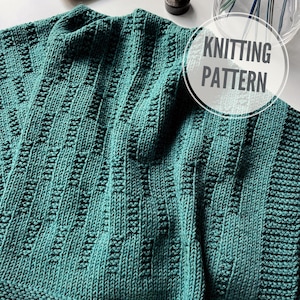 May include: A teal knitted blanket with a textured stitch pattern. The blanket is folded in half and has a "Knitting Pattern" label.