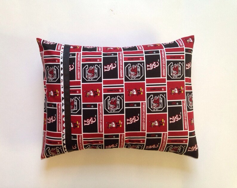 Puede incluir: Una almohada roja y negra con un patr&oacute;n repetido del logotipo de los Gamecocks de la Universidad de Carolina del Sur. El logotipo presenta un gallo con el texto "University of South Carolina" y "Gamecocks".