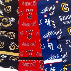 May include: A collection of five fabric squares with different baseball team logos. The logos include the Los Angeles Angels, the San Diego Padres, and the Los Angeles Rams. The fabric squares are all different colors, including red, blue, black, and yellow.