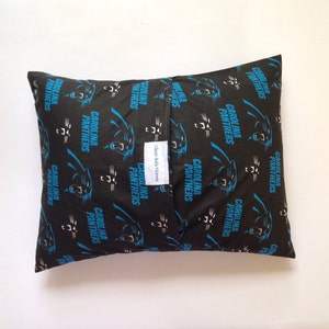 Puede incluir: Una almohada negra con un patr&oacute;n de logotipo de los Carolina Panthers. La almohada est&aacute; hecha de tela y tiene una cremallera. El texto "Classic Baby Items" est&aacute; impreso en una etiqueta blanca unida a la almohada.