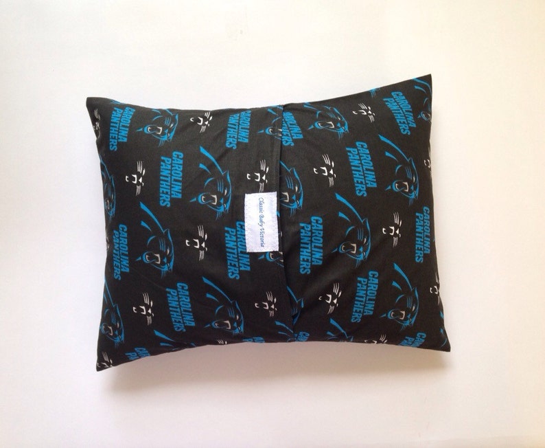 Puede incluir: Una almohada negra con un patr&oacute;n de logotipo de los Carolina Panthers. La almohada est&aacute; hecha de tela y tiene una cremallera. El texto "Classic Baby Items" est&aacute; impreso en una etiqueta blanca unida a la almohada.