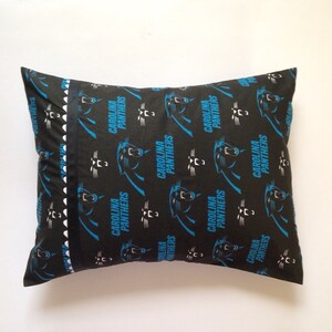 Puede incluir: Una almohada negra y azul con un patr&oacute;n repetido de logotipos de los Carolina Panthers. La almohada tiene un ribete blanco y negro.